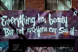 A brick wall with graffiti that reads “Everything has beauty but not everyone can see it” in large, stylized white lettering on a purple background.