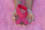 hands holding a pink ribbon.