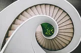 a curving beige stairway with a center filled with green plants.