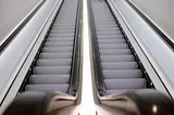 A person riding up an escalator seemingly about to enter a small hole.