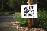 A simple sign put up on someone’s lawn. It says: You Are Worthy Of Love