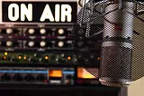 A broadcast microphone with filter is with an “On Air” sign and control board.