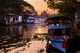 weathered Boats anchored on the banks of a river in India at sunset. a blue one in the foreground.