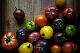 Multiple varieties of tomato, of varying and vibrant colors, are on a wooden table.