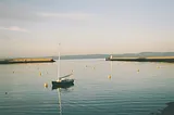 A photograph of Granton Harbour on the Firth of Forth waterfront, in the north of Edinburgh, on a beautiful clear day with a small boat in the foreground.