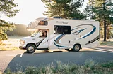 An RV sitting on a street by a river and trees