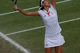 A tennis player, clad in white, prepares to serve.