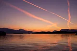Photo of airplane contrails over a lake at sunset