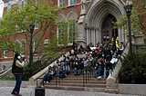 Protesting students sit on the stairs of a building.