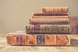 Stack of old, pale books on their sides, longest on bottom, shortest on top.