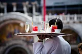 The back of a waiter holding a tray full of glasses, including water, wine and two cocktails.