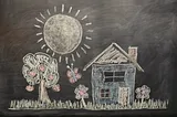 Chalk drawing on a blackboard presumably by a child, of a house with a yard, trees, and the sun prominently shining in the sky.