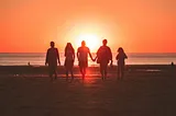 a group of people walk towards a sunset on a beach
