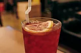 a clear glass filled with a colored liquid and ice with a slice of lemon on top and a straw in the glass