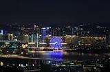 The skyline of Shenzhen that prominently features a neon purple Ferris wheel casting a throw of light over water
