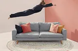 A woman playing Superman over a couch.