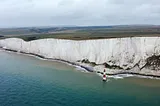 The long stretch of Beachy Head’s cliffs dwarfs the red and white lighthouse in the sea below.