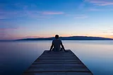 Image describe a person sitting on the middle bridge of riverbed.