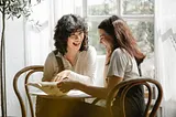 Two women sharing a positive conversation in a bright white room while looking at and discussing a document in front of them