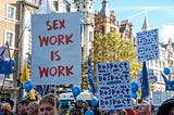 People holding up pro-sex worker signs in a crowd.