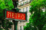 Parisian metro stop in front of lush trees and an apartment building