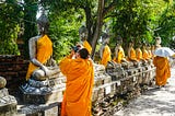 Buddhist monk taking a picture of a Buddha statue. Photo by AXP Photography on Unsplash