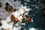 Suntanned women and men having a pool party. They are drinking cocktails and the pool is covered with foam.