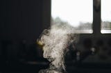 A white pot on the stove with steam coming out of it.