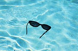 Sunglasses floating in bright blue water.