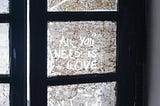 A dirty window with “All you need is love” written on it.