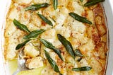 An oval casserole dish of gnocchi gratin garnished with crispy sage leaves.