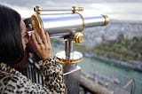 Woman looking through standing binoculars at city view
