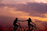 Silhouette of a man and woman on bikes against a cloudy sky background for my Love-Lie poem