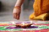 Traditional Indian patterns called ‘rangoli’ being made with colours along with a display of few lit earthen lamps.