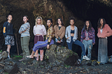 The cast of The Wilds poses on a rock with intense looks on their faces.