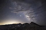 A nearly silhouetted peak under the Milky Way partially obscured by clouds.