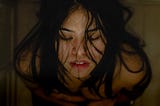 Woman with dark hair and closed eyes, leans the back of her head on the glass shower door.