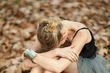 A woman sitting on the ground, her arms wrapped around her knees and her head down.