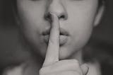 Woman with finger over lips quieting a lie.