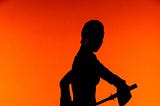 Silhouette of a female warrior is seen weilding a sword, shown against a high-contrast orange background.