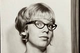 Headshot of author at 22, wearing horn rim glasses, sleeveless dress, and an updo hairstyle with bangs