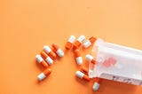 Prescription drugs on an orange background with a pill bottle.