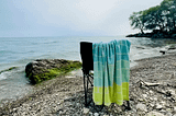 Beach day, a beach chair on the water’s edge, towel, pebbly shoreline, and water views | © pockett dessert