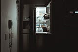 An open, lit refrigerator in a dark kitchen waiting for a fridge forage session to find your next meal.