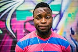 A man stands in front of a colourful graffiti wall, looking playfully confused.