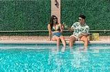 A guy and a girl sitting and relaxing with drinks in a swimming pool