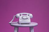 Rotary phone on a barstool with a pink background