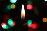 Black background with brilliant green and red lights and a single candle flame in the center