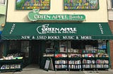 Green Apple Books and Music shop—a store with a green awning, a green neon sign, and cases of books on the sidewalk.