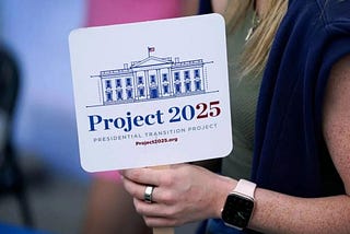 The hand and arm of a white woman holding a Project 2025 sign.